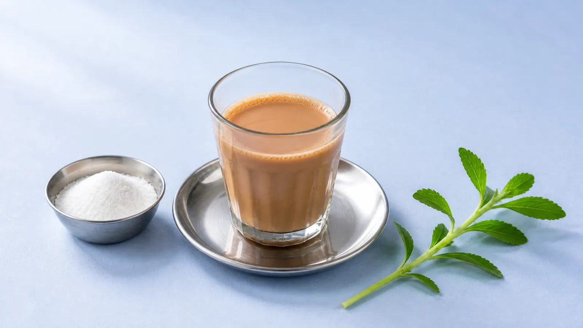 स्टील की तश्तरी पर दूध वाली चाय, पास में ताज़ी स्टेविया पत्तियों की टहनी और सफ़ेद स्वीटनर पाउडर की छोटी स्टील कटोरी