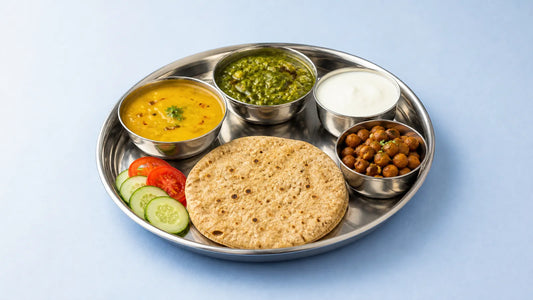 A steel thali with a roti, dal, palak sabzi, curd, chana and sliced cucumber and tomato