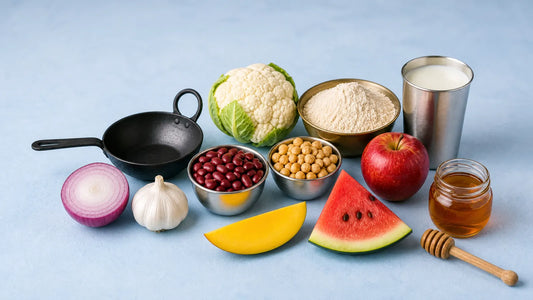 Onion, garlic, rajma, chana, atta, milk, apple, mango, watermelon and honey on a pale counter with a kadai