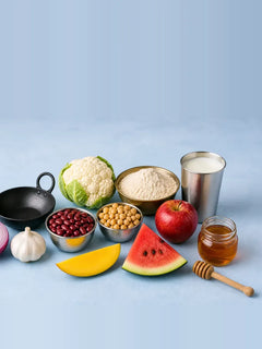 Onion, garlic, cauliflower, beans, atta, milk, mango, watermelon, apple and honey around a kadai on a pale blue table