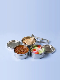 Three open steel tiffin boxes side by side with rotis, rajma and a cucumber, tomato and onion salad, lids beside them