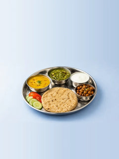 A steel thali with a roti, dal, palak sabzi, curd, chana and sliced cucumber and tomato